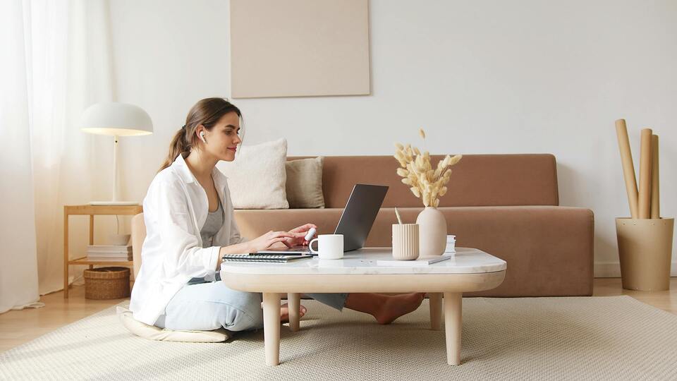Woman working on a laptop in a cozy, minimalistic living room.