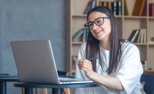 Smiling woman with glasses using a laptop in a library.