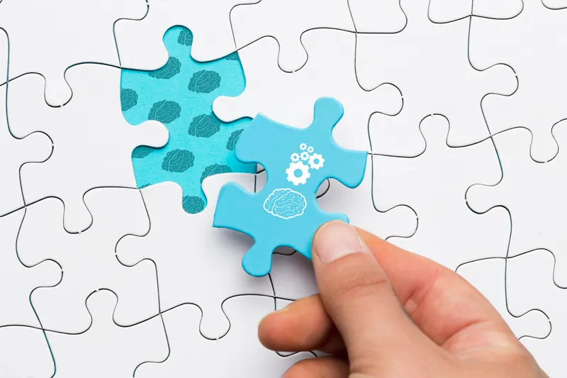 Close up human hand holding blue puzzle piece with brain