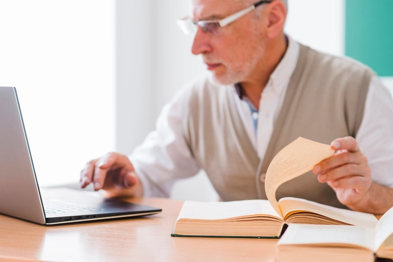 Senior professor working with laptop while holding page book